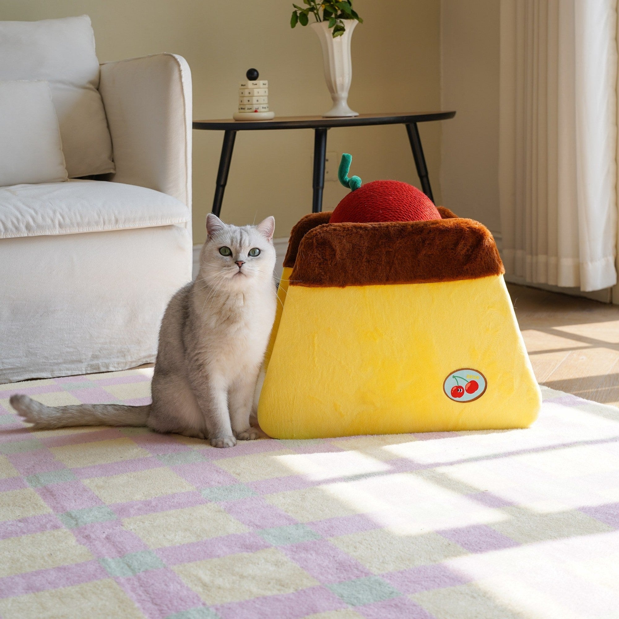 Cat sitting beside the ZEZE Cherry Pudding cat scratcher in a sunny living room