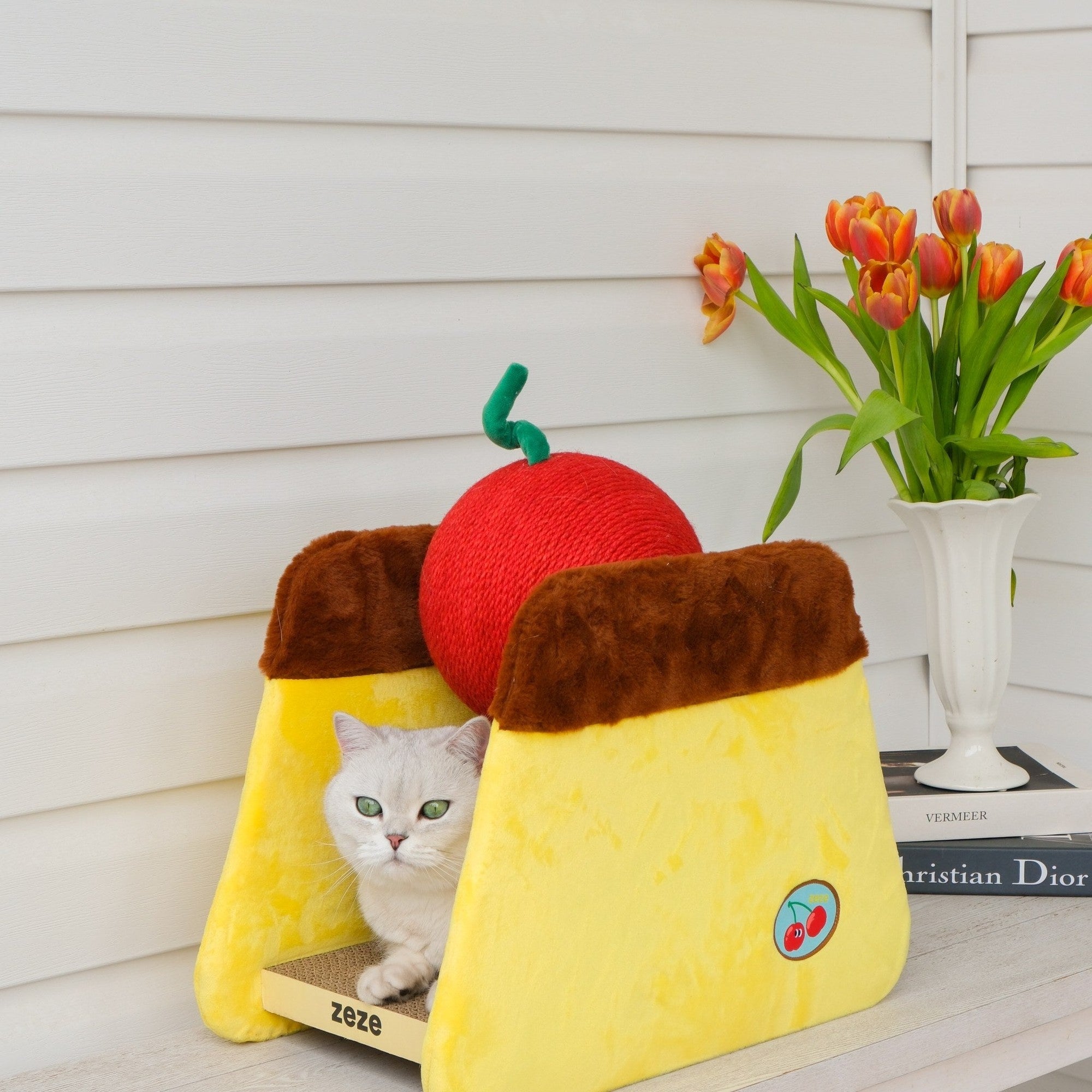 Cat peeking out from inside the pudding scratcher next to tulips