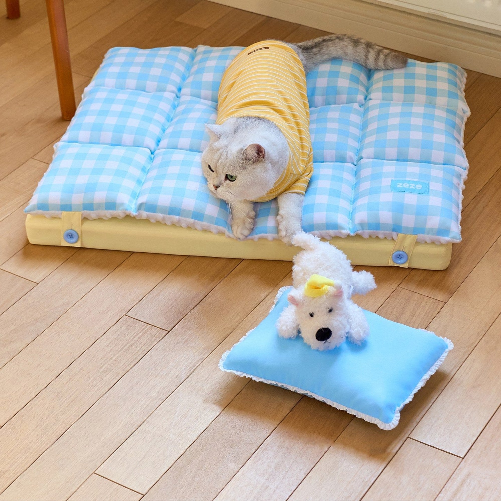 Cat lying on the gingham nap mat next to the pillow and plush puppy
