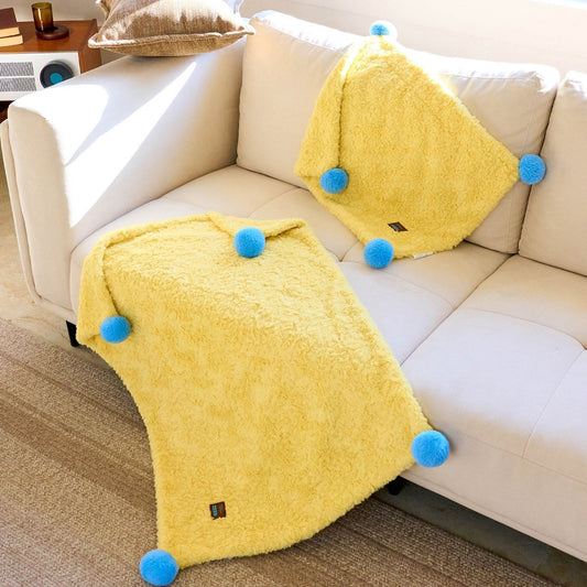 Medium and Large ZEZE pompom blankets on a sofa