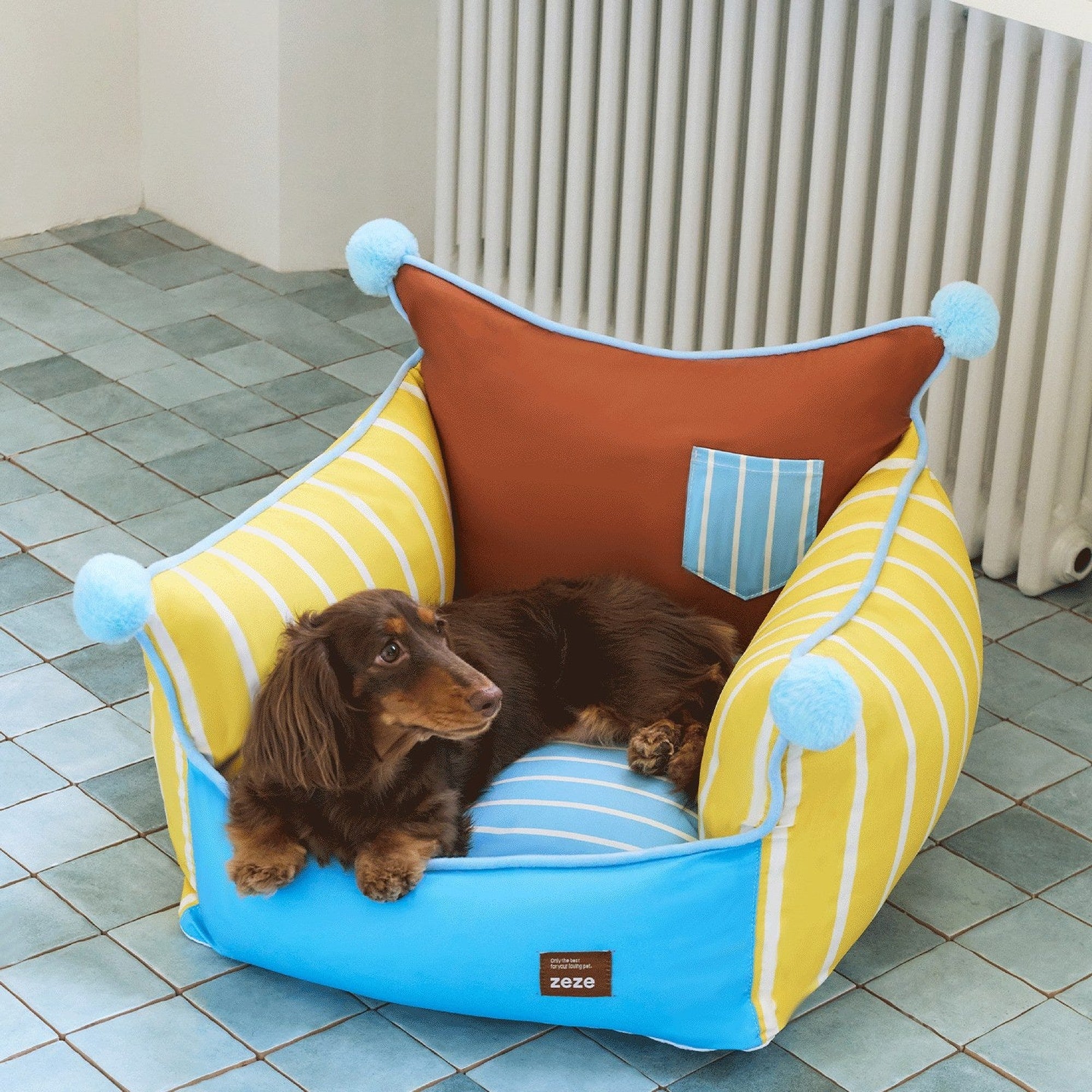 Dachshund curled up in the pompom pet sofa beside a radiator