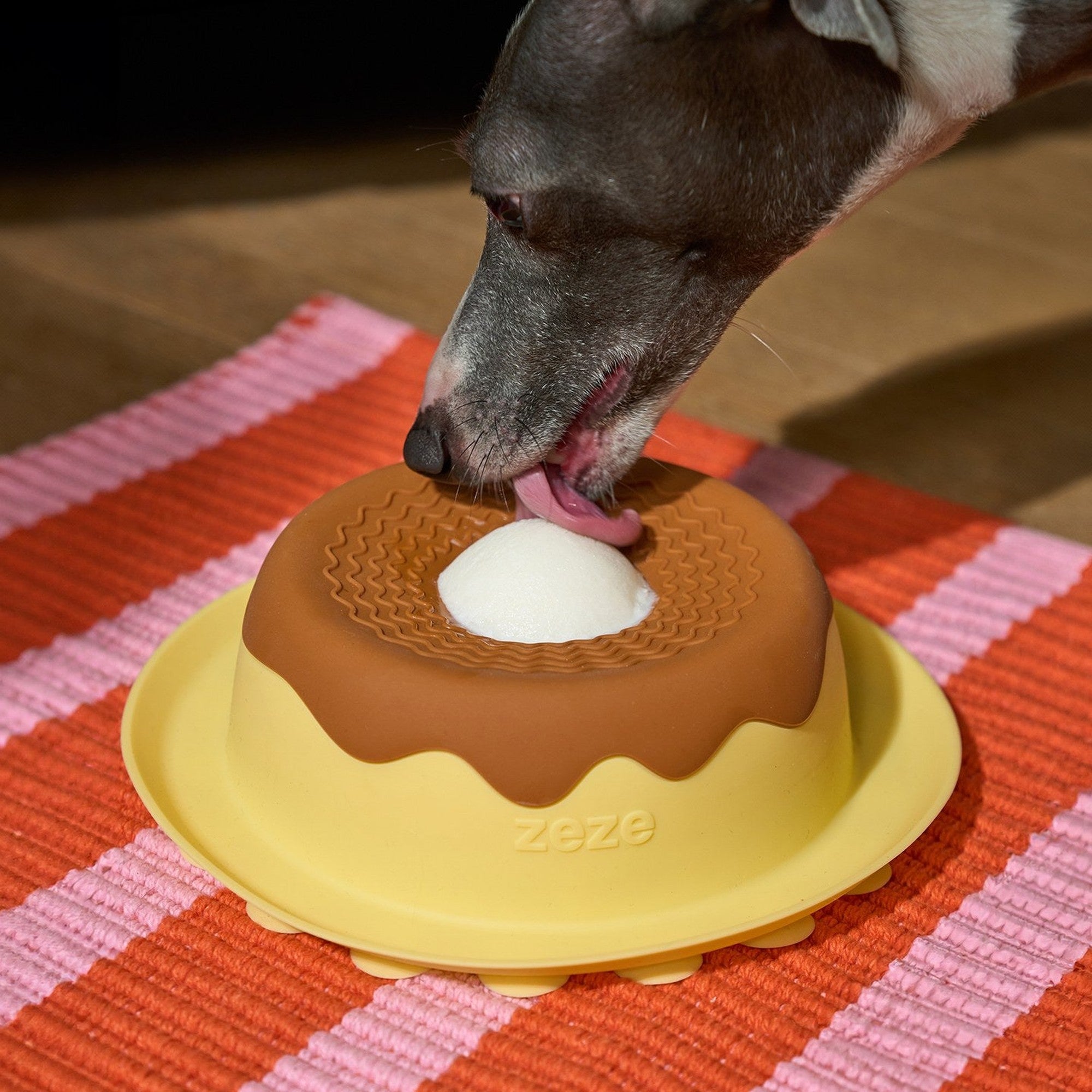 Dog licking the ZEZE Pudding Lick Bowl on a striped mat