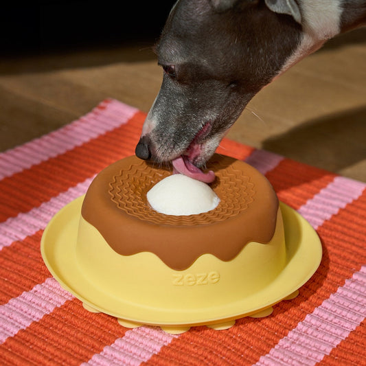 Dog licking the ZEZE Pudding Lick Bowl on a striped mat