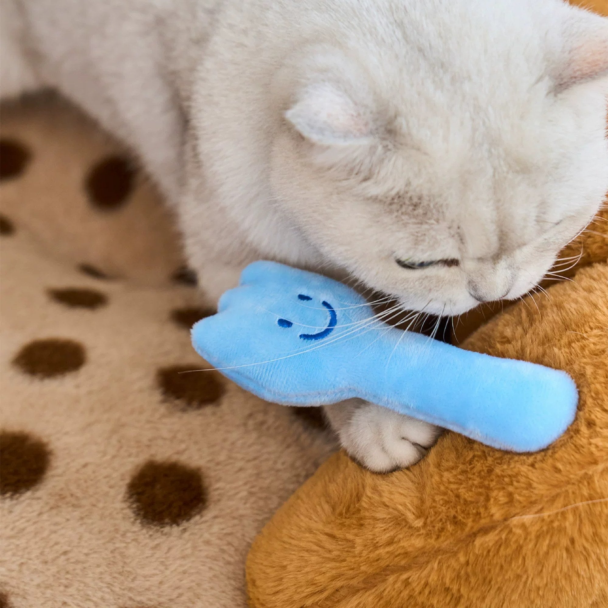 Cat cuddling the blue fork plush toy included with the ZEZE Croissant pet sofa